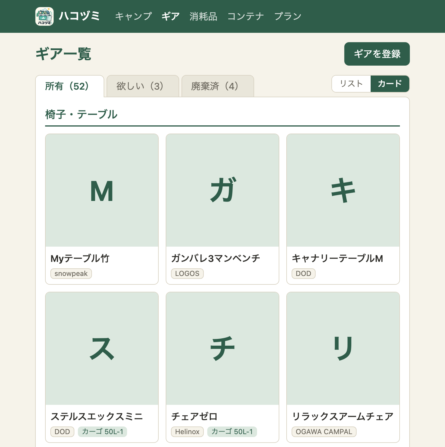 ギア一覧のカード表示。状態のタブの右に「リスト」「カード」の切り替えがあり、「カード」が選ばれている。「椅子・テーブル」の見出しの下に、カードが3列で並ぶ。画像のないギアは、淡い緑の背景に製品名の頭文字（M、ガ、キ など）。その下に製品名と、メーカー・コンテナのバッジ